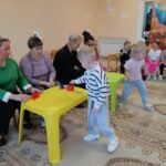 Дети и взрослые в комнате детского сада за малыми столиками с игрушечной посудой — праздничное занятие и игры