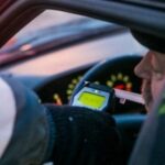 Сотрудник полиции проводит проверку водителя алкотестером через открытую дверь/окно автомобиля
