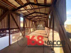Пустой крытый переход с ржавым металлическим каркасом, решётчатым полом и повреждённой обшивкой