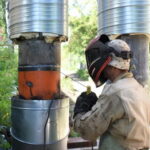 рабочий в сварочной маске выполняет работу на изолированных вертикальных тепловых трубах на улице