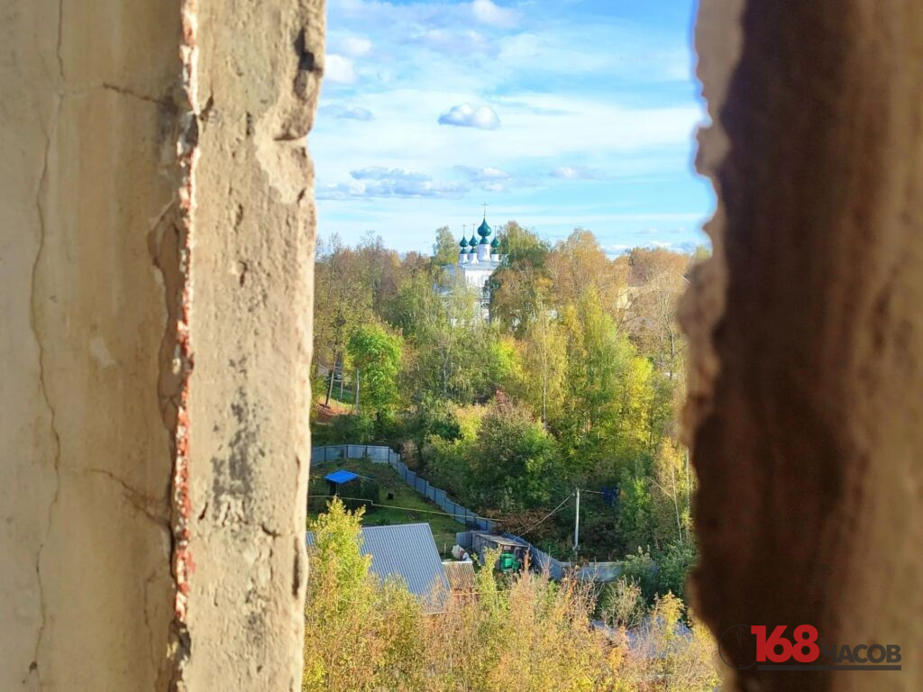 Церковь с зелёными куполами среди осенних деревьев, видимая через узкий проём в стене