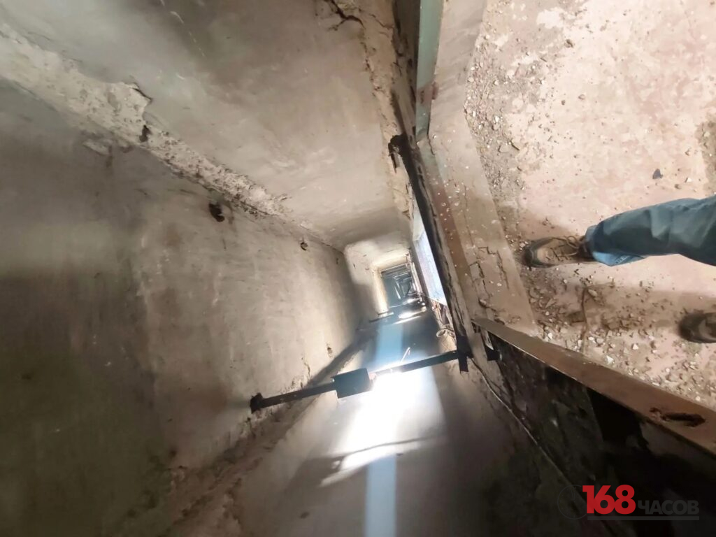 Вид сверху в глубокую шахту внутри заброшенного здания; у края стоят ноги человека