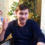 мужчина сидит за гримёрным столиком перед зеркалом; расчёски, карточки и праздничная гирлянда на заднем плане