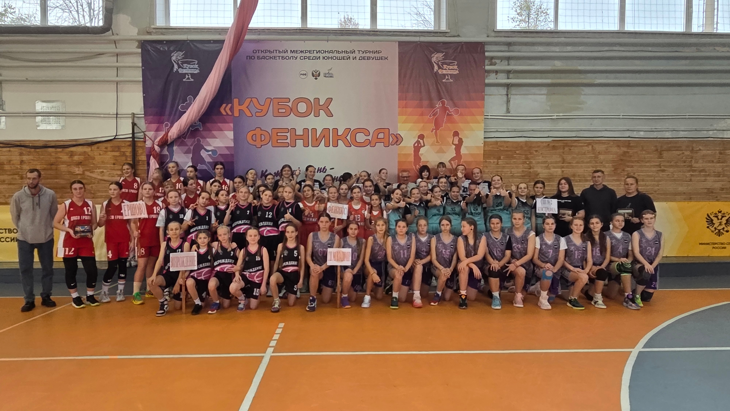 Групповая фотография юношеских баскетбольных команд в спортивном зале на фоне баннера «Кубок Феникса»