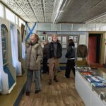 Группа студентов осматривает экспозицию и стенды в небольшом музее/выставочном зале