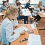 Ученики в кабинете пишут экзамен; на столах экзаменационные бланки, номера парт и паспорт.