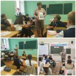 взрослая женщина стоит перед школьной доской и держит книгу с портретом; дети сидят за партами в классной комнате, на столах учебники и тетради