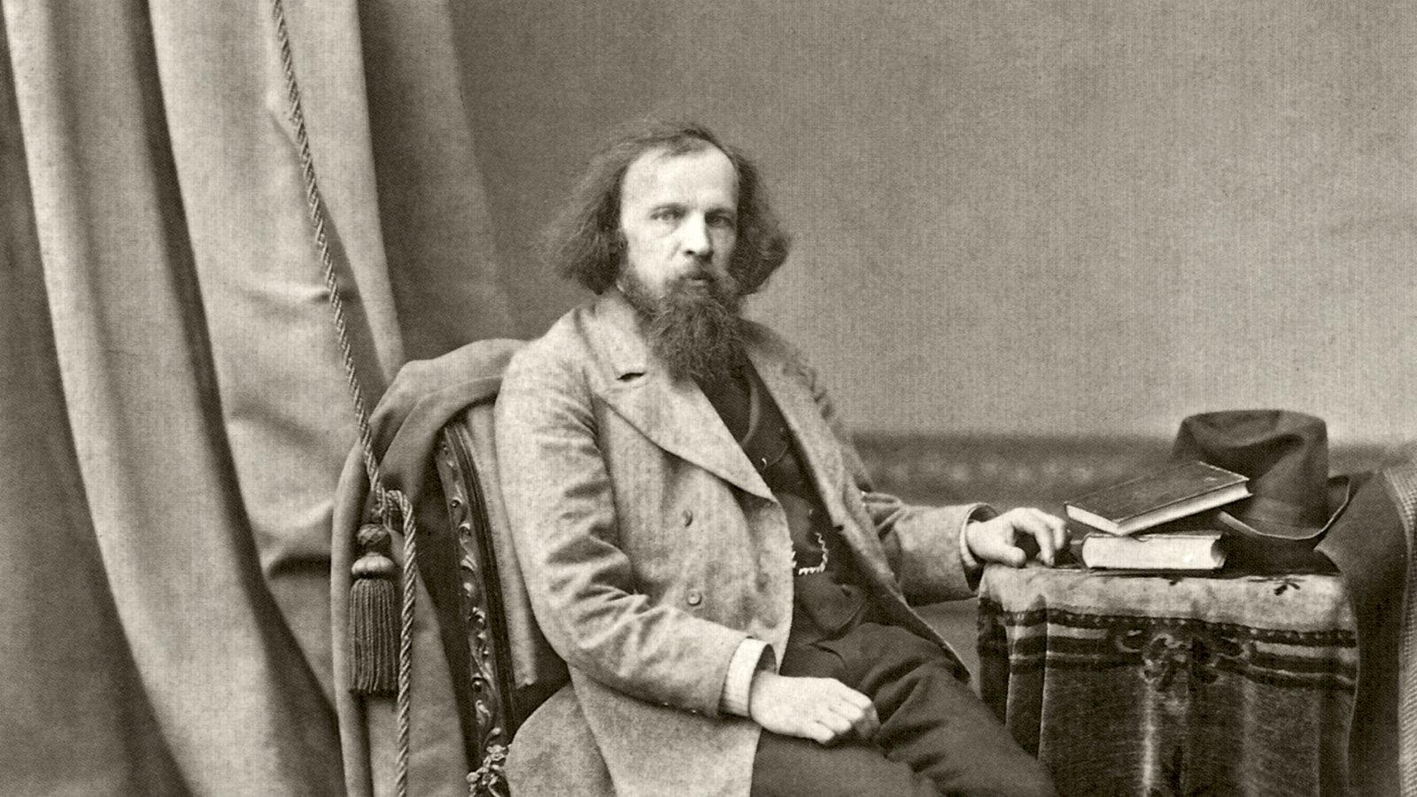 Дмитрий Менделеев сидит рядом со столом с книгами. Фотография Андрея Карелина