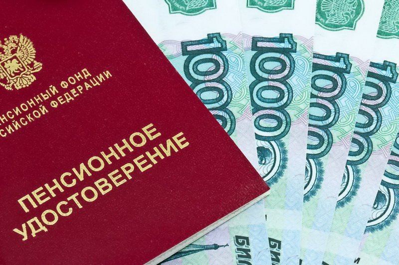 Пенсионное удостоверение на фоне стопы купюр номиналом 1000 рублей.
