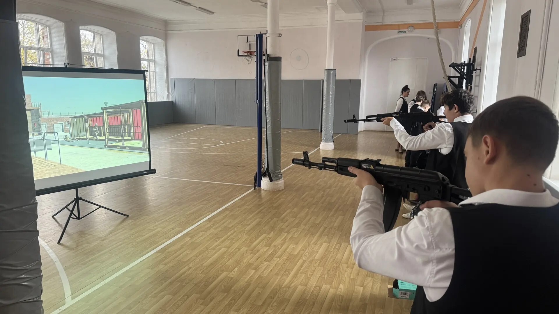 Школьники в спортивном зале стреляют из электронных винтовок по изображению на проекционном экране