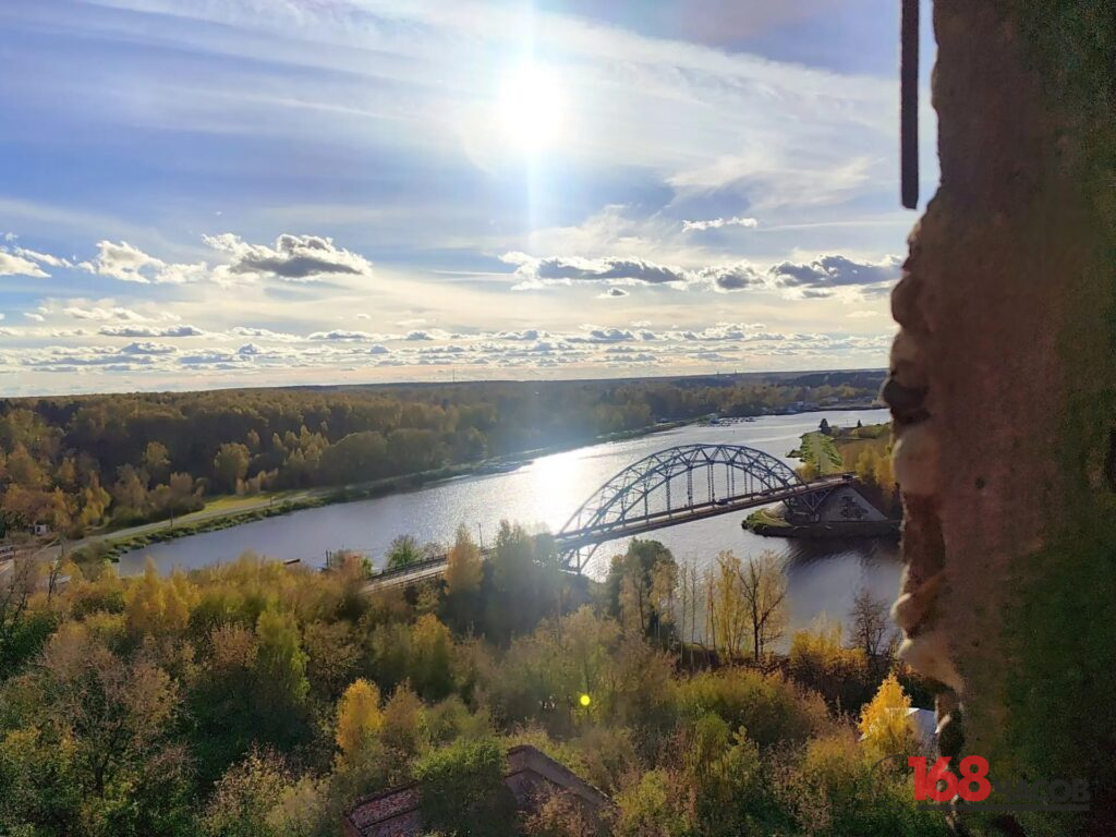 Вид с высоты на арочный железнодорожный мост через реку и осенний лес под облачным небом