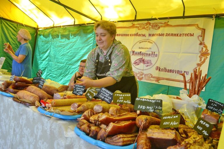 торговая палатка с мясными деликатесами на ярмарке, продавец за столом с ценниками