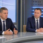 двое мужчин в деловых костюмах сидят за студийным столом во время интервью/дискуссии