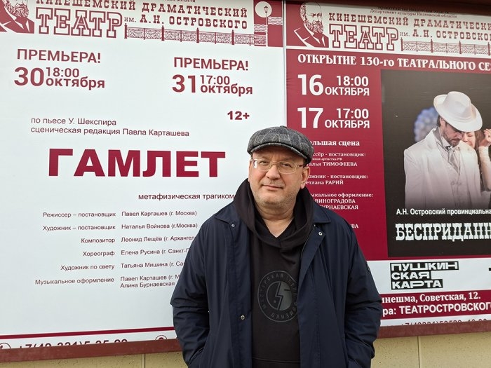 Мужчина на фоне афиши спектакля «Гамлет» с крупной надписью и датами премьер 30 и 31 октября у оформления театра.