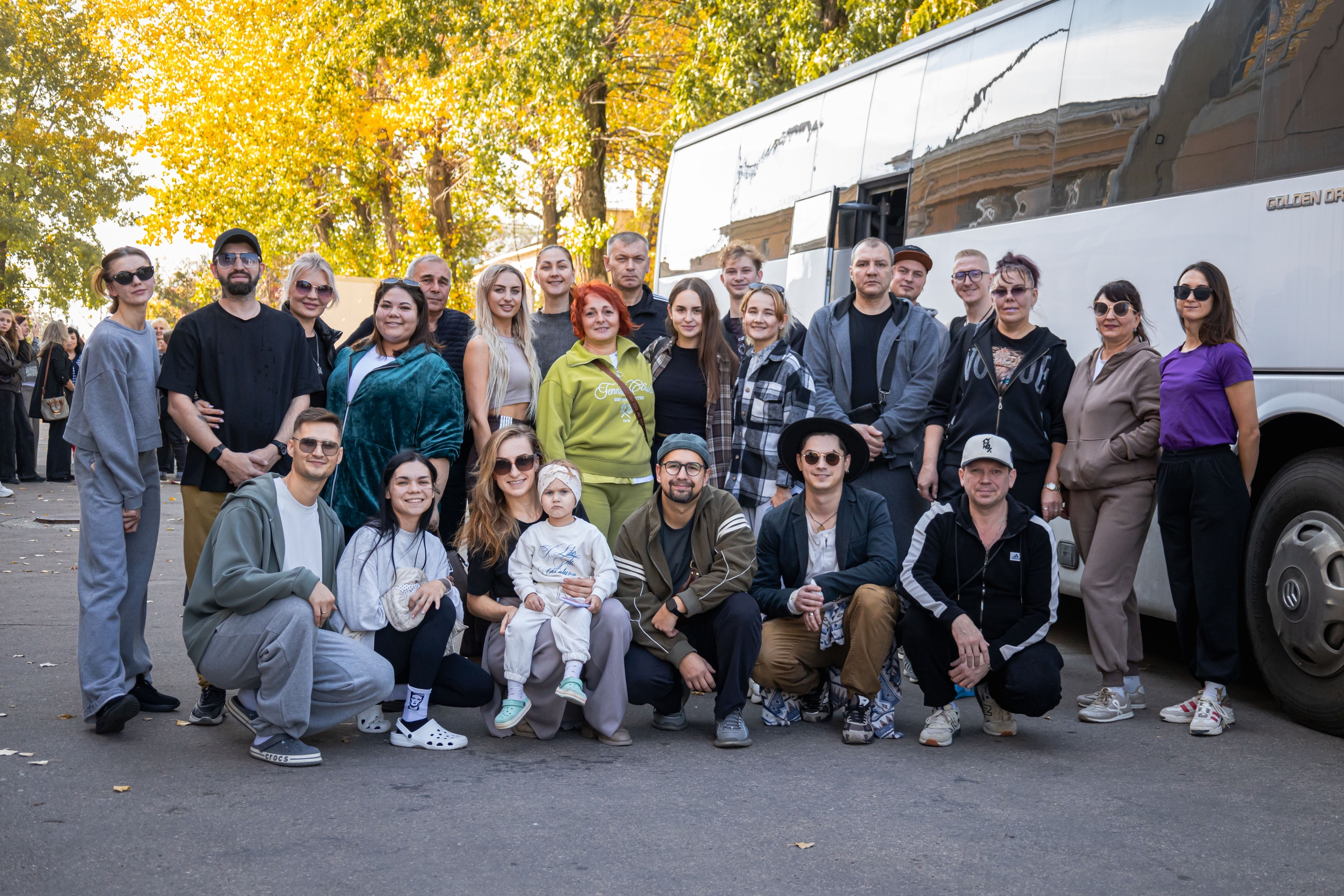 Групповая фотография труппы/коллектива у белого пассажирского автобуса на улице, осенний день.
