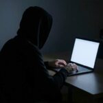 Человек в капюшоне за ноутбуком в темной комнате