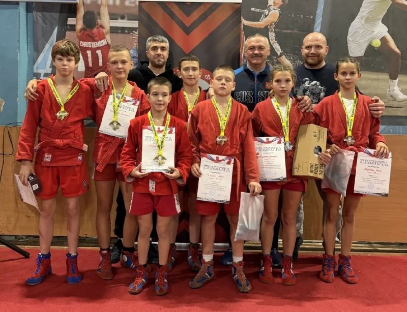 Группа юных самбистов в красной форме с медалями и грамотами в спортивном зале