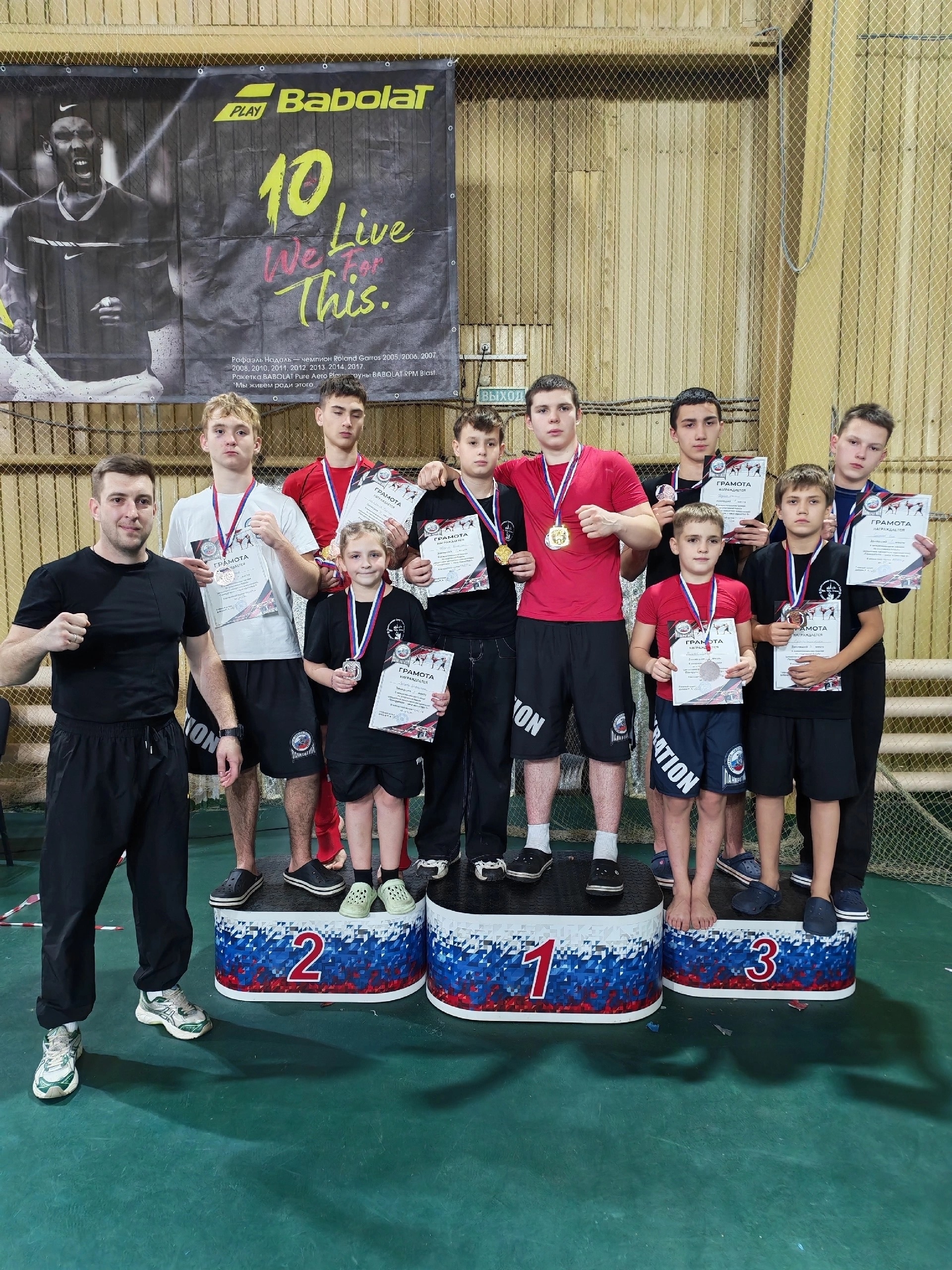 Группа юных спортсменов в спортивном зале на пьедестале (1,2,3) с медалями и грамотами.