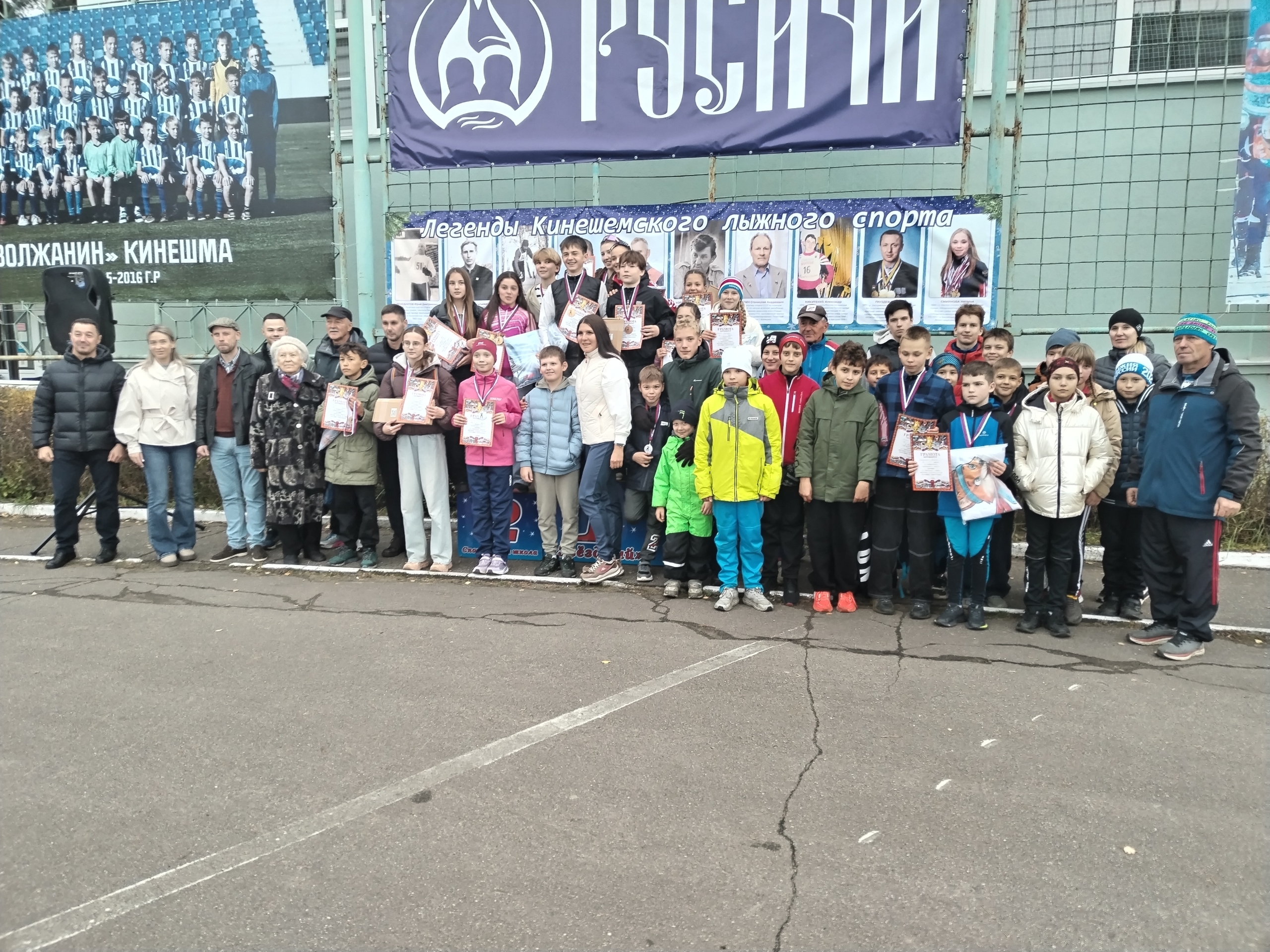 Групповое фото юных спортсменов с медалями и грамотами на фоне баннеров «Легенды Кинешемского лыжного спорта» и «Волжанин Кинешма».
