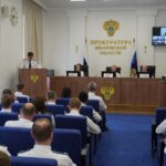 Зал заседаний прокуратуры с трибуной, гербом и надписью «Прокуратура Ивановской области», люди в светлой форме в аудитории.