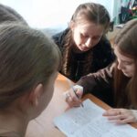 несколько школьниц за партой в классе, работают в группе с листами бумаги и ручкой