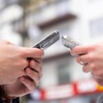 Руки двух человек, держащих смартфоны на фоне улицы