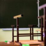 пустой школьный класс: парты со стульями, поднятыми наверх, зелёная доска и учебный плакат на стене