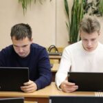 Двое молодых людей за партами работают на планшетах/ноутбуках в учебном классе/кабинете