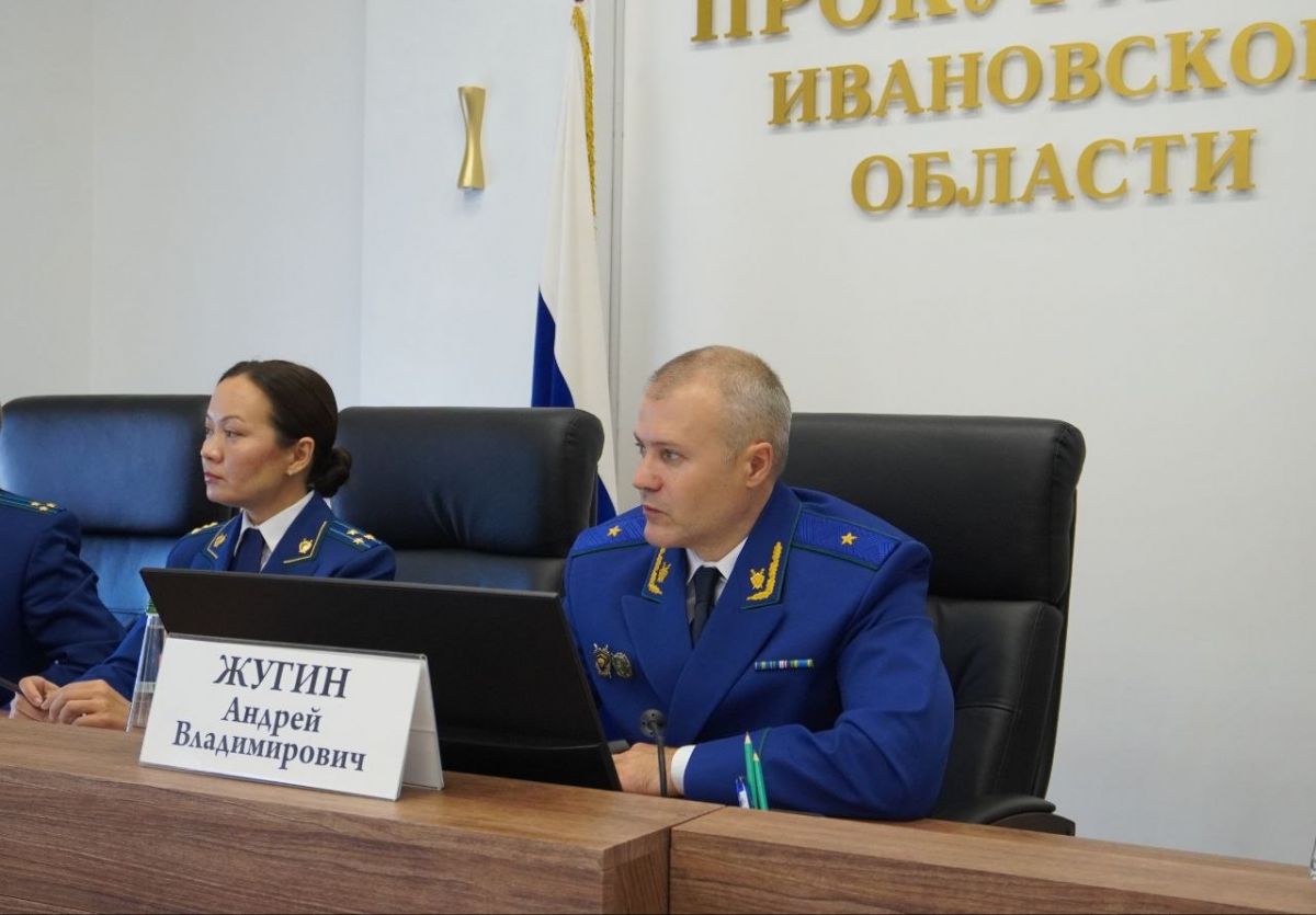 Двое людей в синей форменной одежде прокуратуры сидят за столом в кабинете с золотой надписью на стене «Ивановской области».