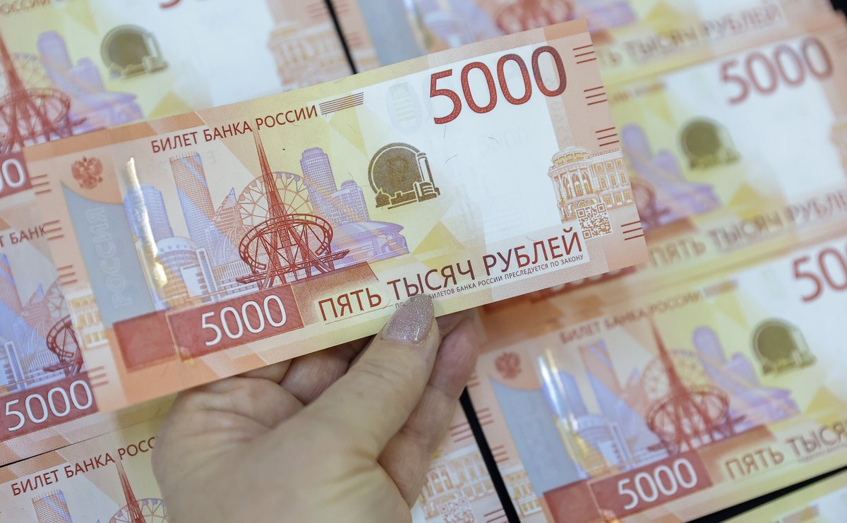 Рука держит купюру 5000 рублей на фоне нескольких таких купюр