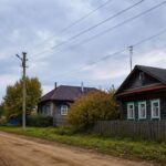 Просёлочная улица в селе: деревянные дома, заборы, опоры и линии электропередачи