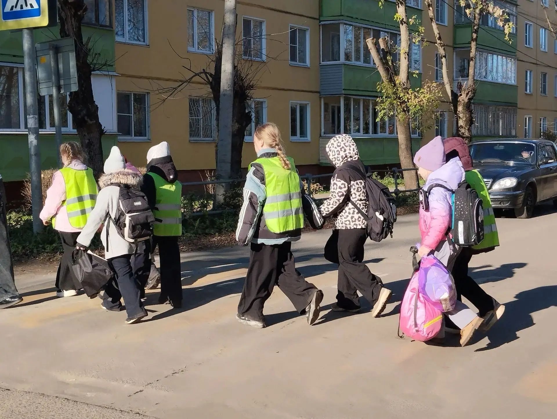 Группа младших школьников в световозвращающих жилетах переходит дорогу по пешеходному переходу, у детей рюкзаки.