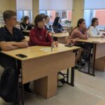 старшеклассники сидят за лабораторными партами в кабинете химии и слушают занятие