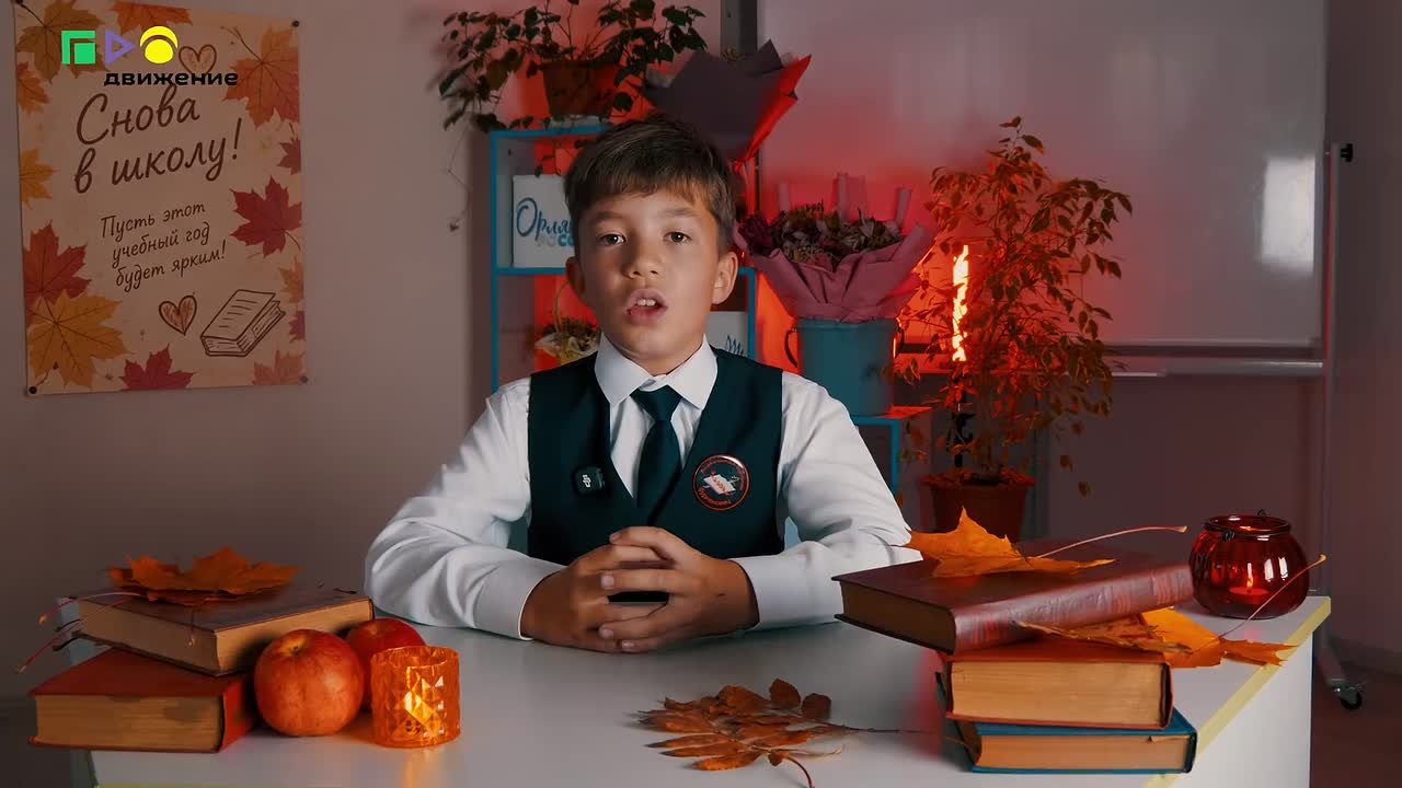 Школьник в форме сидит за столом с книгами, осенними листьями и яблоками; на заднем плане осенняя декорация и постер «Снова в школу!»