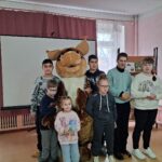Группа детей и ростовая кукла (белочка) в детском отделе библиотеки на фоне проекционного экрана и книжной полки.