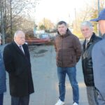 Группа мужчин обсуждает работы на улице на фоне ограждённого раскопа и строительной техники.
