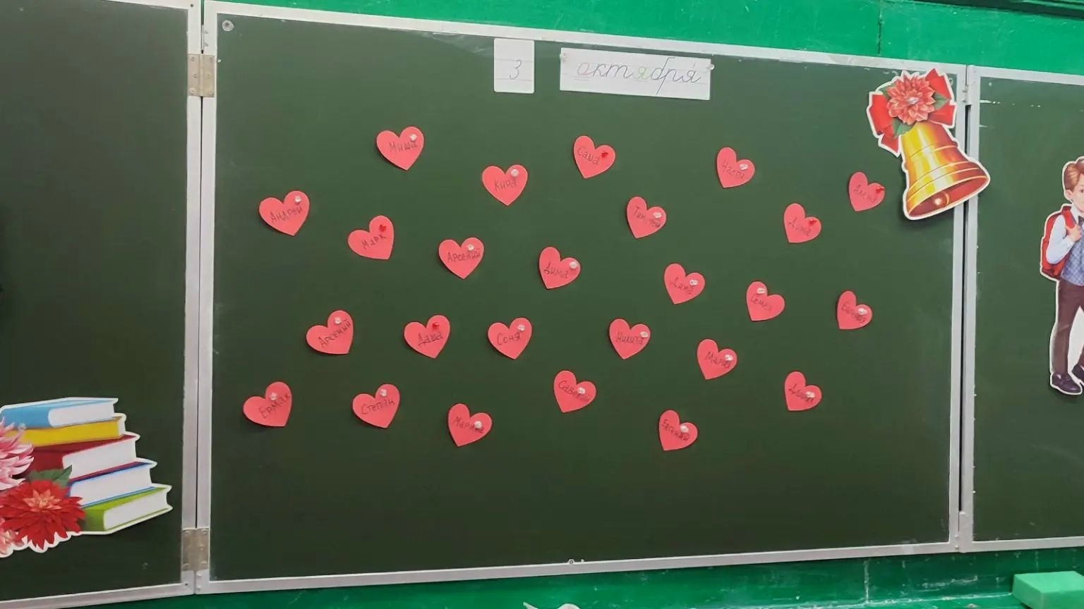 классная (школьная) доска, на ней прикреплены красные бумажные сердечки с именами, наверху бумажная надпись «3 октября», декоративные вырубки (колокольчик, стопка книг, фигурка ребёнка)