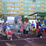 Дети и воспитатели на новой спортивной площадке детского сада: травмобезопасное покрытие, обручи, конусы и игровые аксессуары.