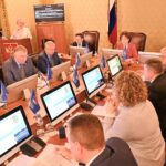 Заседание чиновников за столом с мониторами и флагами