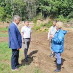 Четверо человек на выровненном земляном участке у лесного склона — осмотр территории с признаками земляных работ.