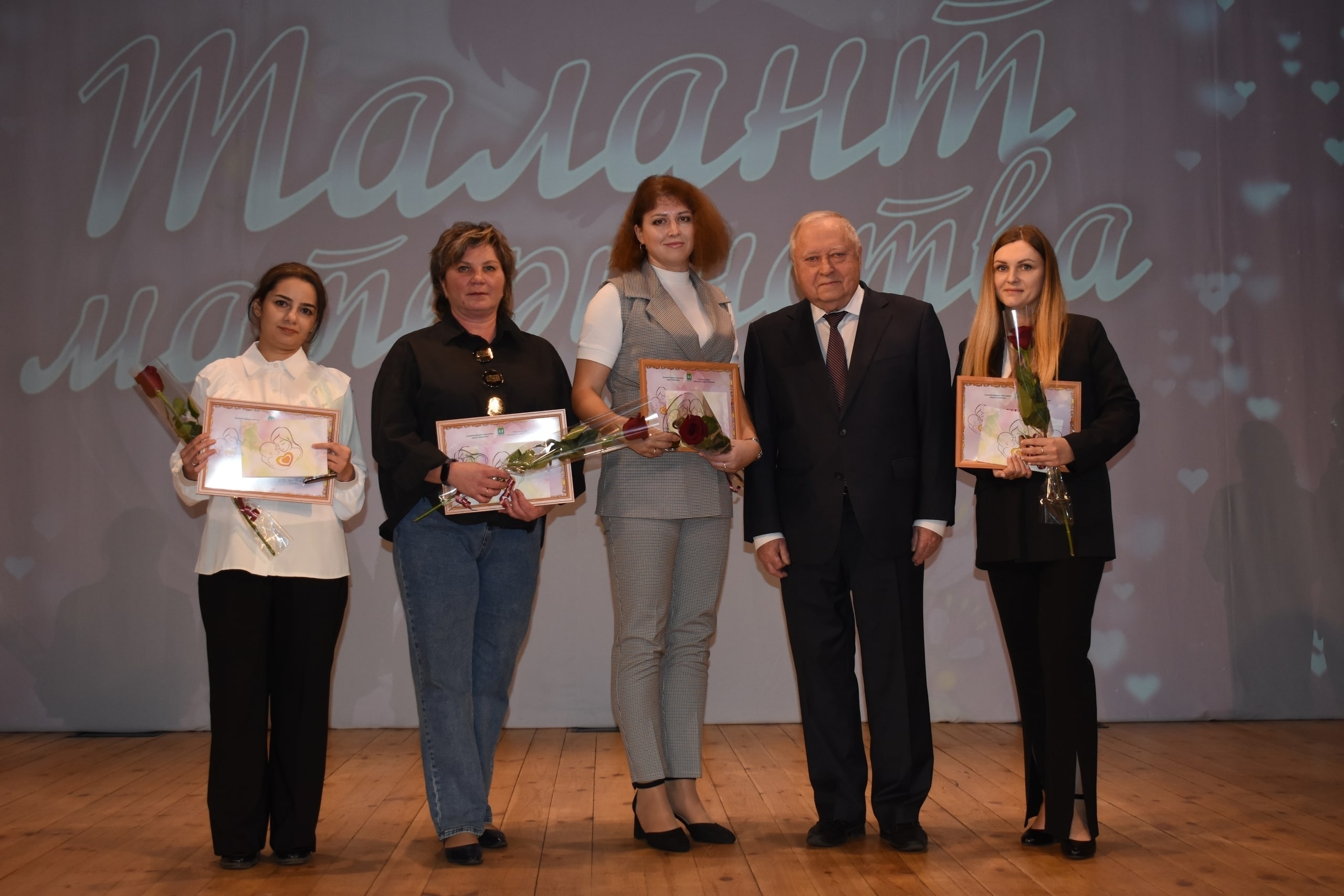 На сцене несколько человек держат дипломы и розы на фоне баннера с надписью «Талант материнства».
