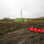 палаточный лагерь на поле с оранжевыми контрольными флажками ориентирования и красным баннером «СТАРТ»