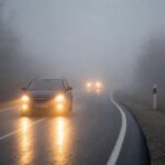 Автомобиль(и) на шоссе в сильном тумане, включённые фары и отражение света на мокрой дороге