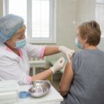 медсестра в медицинской маске вводит инъекцию в плечо пациентки в процедурном кабинете поликлиники
