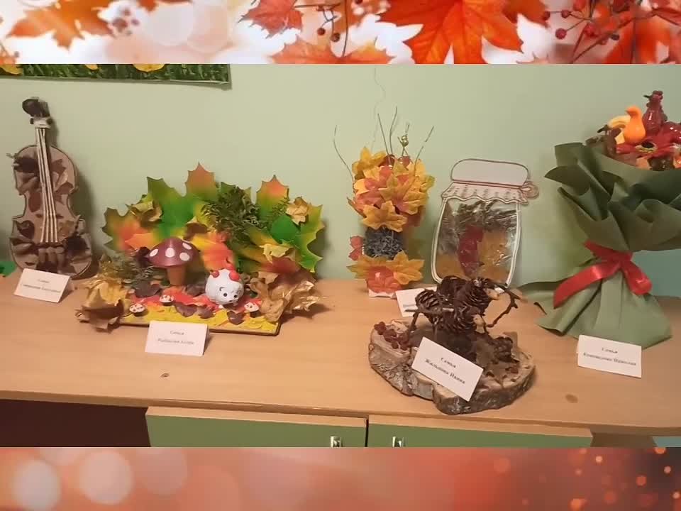 Стол с осенними поделками и композициями (бумажные листья, фигурки, букет), перед ними подписные карточки