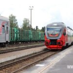 Платформа железнодорожной станции с красным пассажирским поездом и товарными вагонами, гружёными бревнами