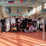 Групповая фотография школьников и взрослых в спортивном зале: участники стоят и сидят на паркете на фоне баскетбольного кольца и плаката с надписью «ТУРНИР», у некоторых — грамоты и подарочные пакеты.